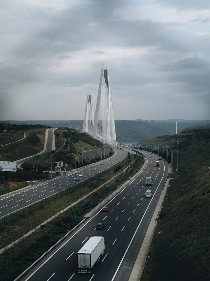 A modern cable-stayed bridge with a highway underneath, showcasing vehicles and cloudy skies.